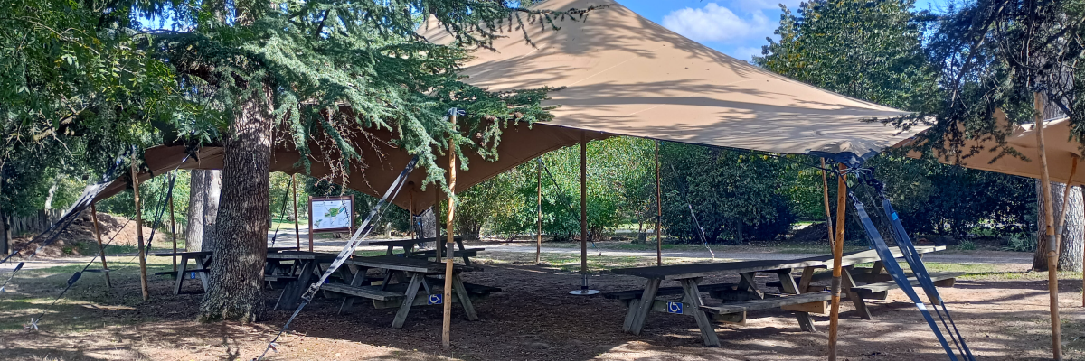 Aire de jeux avec toboggan, balançoire, tables de pique-nique et abris.