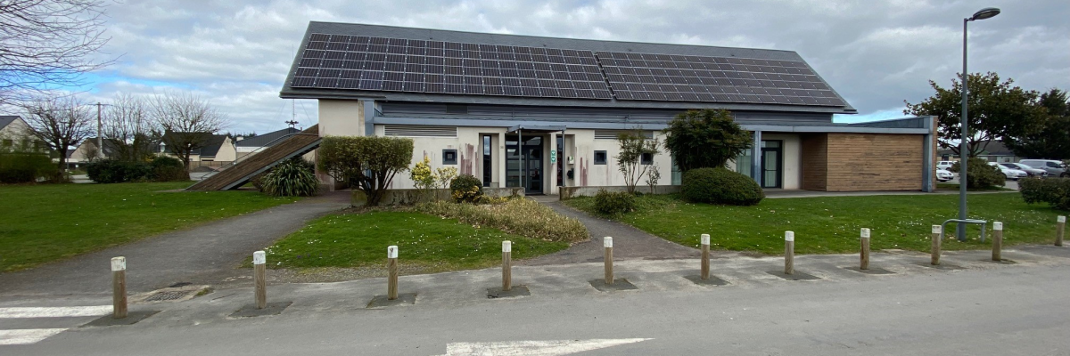 Bâtiment avec panneaux solaires, allée et parking.