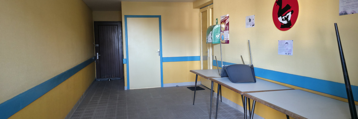 Pièce avec tables, chaises, porte, tableau d'affichage et affiches.