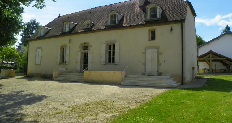 Maison à deux étages avec toit en ardoise, fenêtres à volets et porte d'entrée. Escaliers extérieurs et jardin.