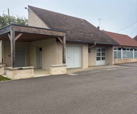 Bâtiment avec toit en tuiles, porte blanche, fenêtres et parking.