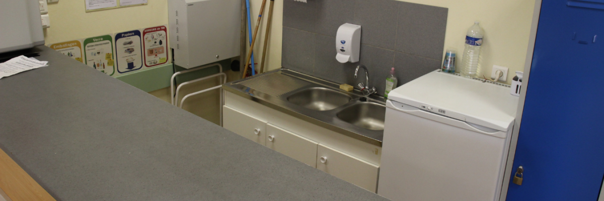 Cuisine avec table, chaises, évier, distributeur de savon, micro-ondes et affiches sur le mur.