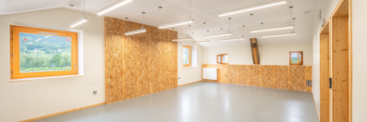 Salle vide avec mur en OSB, porte en bois, fenêtre, éclairage et ventilations au plafond.