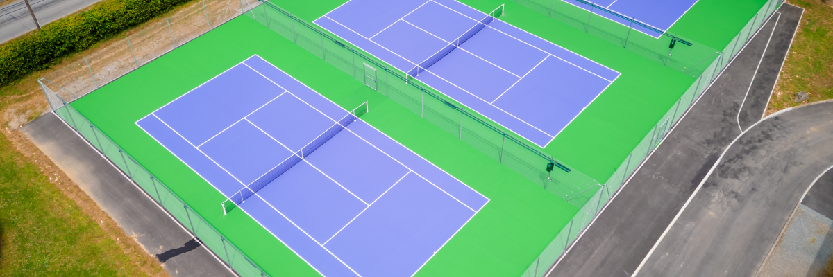 Quatre terrains de tennis avec clôtures, filets et surface verte et bleue.