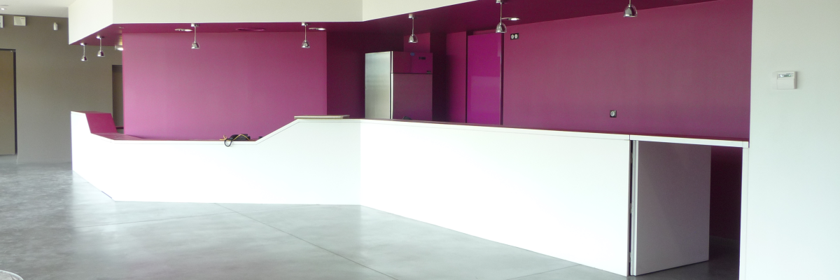 Salle vide avec murs blancs et violets, spots, comptoir blanc et sol gris.