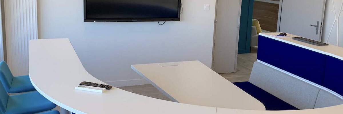 Salle de réunion avec table, chaises, écran et porte avec logo.