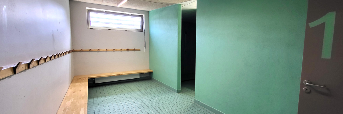 Salle avec banc, sol carrelé, mur vert, porte, fenêtre, éclairage.