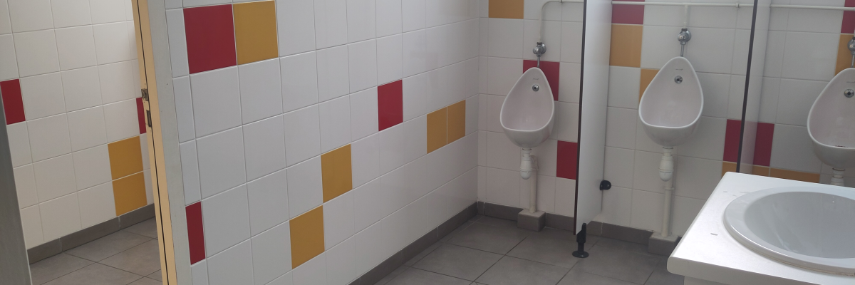 Toilettes avec urinoirs, lavabo, porte et carrelage mural coloré.