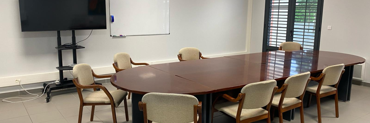 Salle de réunion avec table, chaises, écran, tableau blanc et caméra.