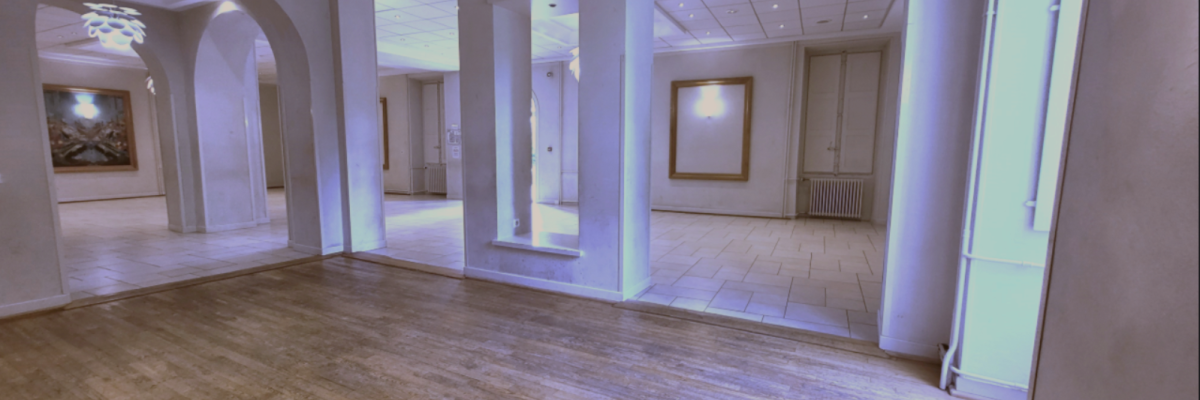 Salle vide avec plafond haut, colonnes, parquet, éclairage et œuvres murales.