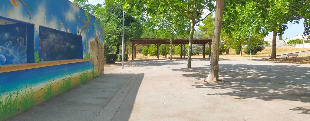 Aire de jeux avec mur coloré, abri et arbres.