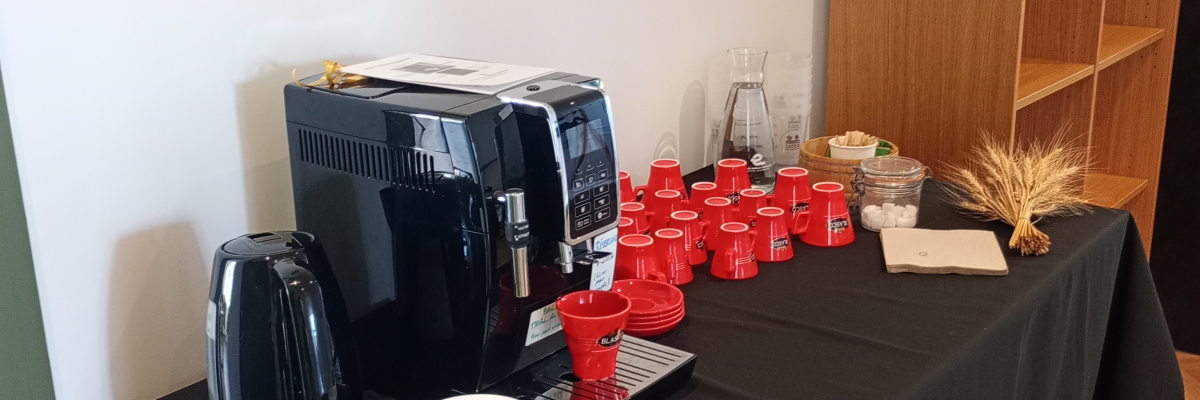 Table avec cafetière, tasses, verres rouges, serviettes et étagères.