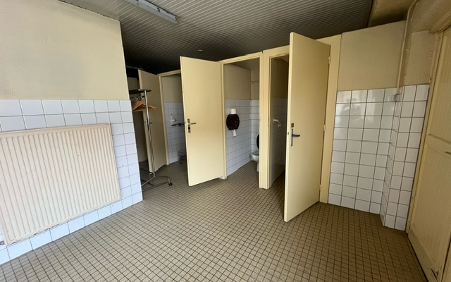 Toilettes avec cabines, urinoirs, radiateur et porte-papier toilette.