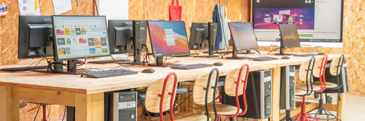 Salle informatique avec table, chaises, moniteurs, écrans, tours et tableau blanc.
