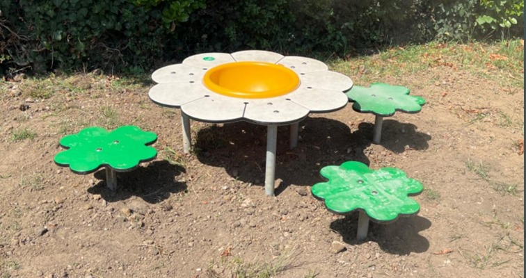 Aire de jeux avec table en forme de fleur, siège jaune et quatre pas en forme de feuilles vertes.