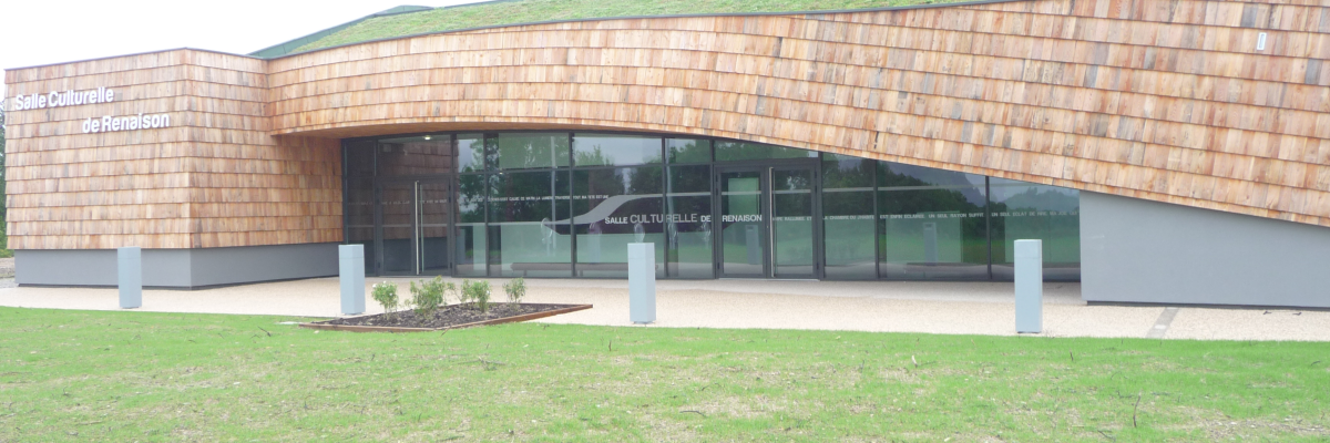 Bâtiment moderne avec façade en bois, toit vert, grandes vitres et pelouse.