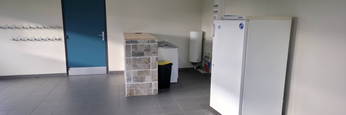 "Pièce avec frigo, meuble en pierre, poubelle, porte bleue et étagères murales."