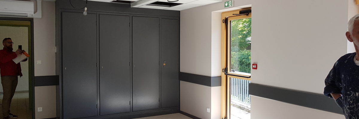 Pièce avec armoires, porte, personne à droite, personne prenant une photo à gauche, boîte au sol.