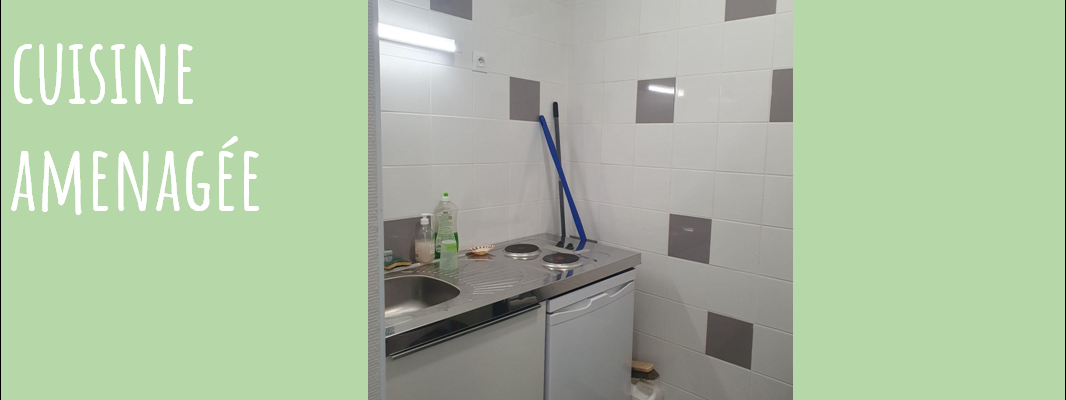 Cuisine avec évier, plan de travail, réfrigérateur et produits de nettoyage.