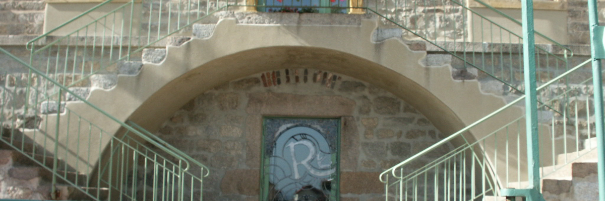Entrée avec escalier, rambarde verte, porte en arc, vitrail et fleurs.