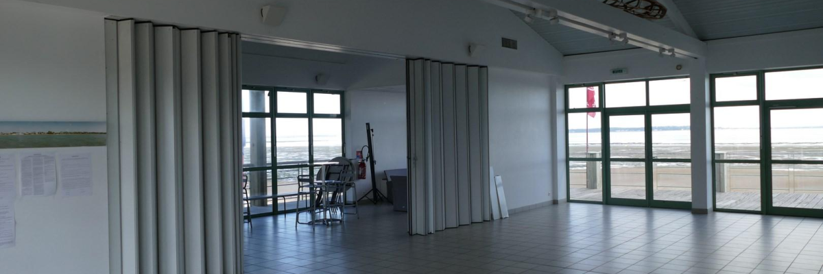 Salle spacieuse avec fenêtres, portes vitrées, rangements et mobilier extérieur.