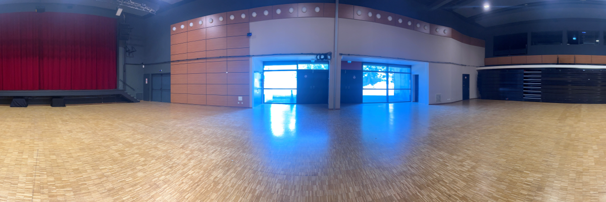 Salle de spectacle avec scène, rideau rouge, parquet, portes et rangements.