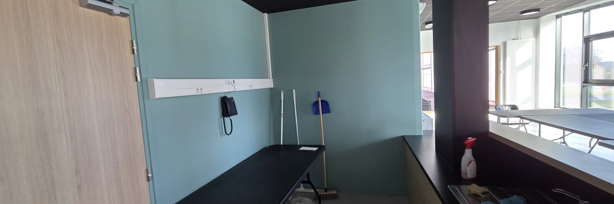 Pièce avec table d'examen, porte, lavabo, miroir, mur vert, plafond sombre et matériel médical.