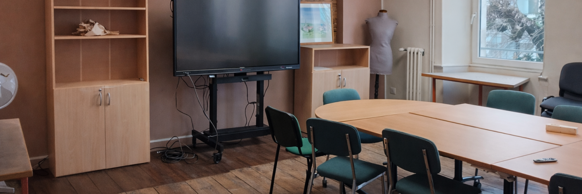 Salle avec écran, table, chaises, étagère, mannequin et radiateur.
