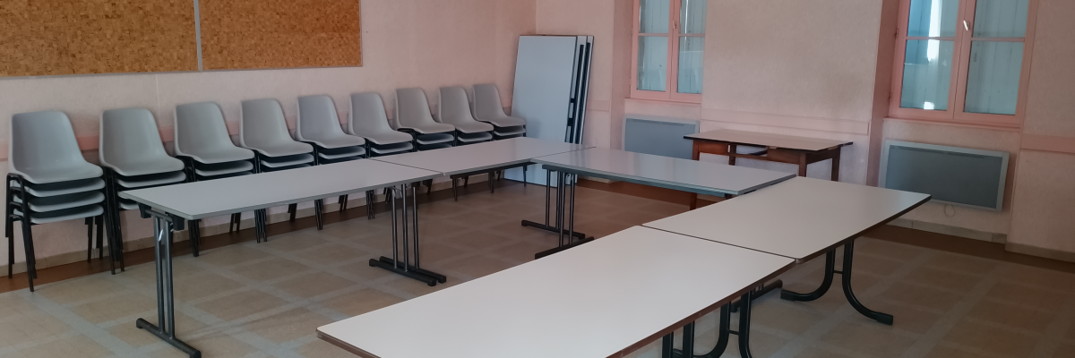 Salle avec tables, chaises, tableau blanc, tableau en liège et radiateur.