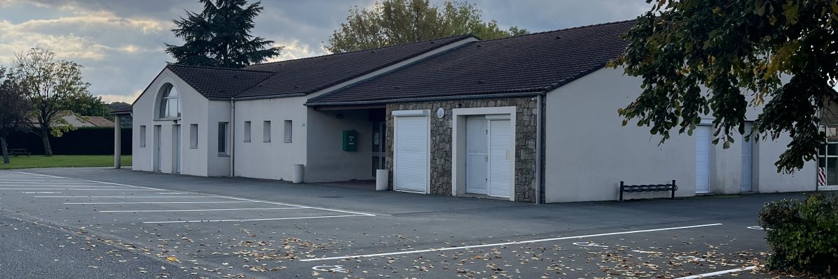 Bâtiment blanc, stationnement asphalte, arbres, nuageux.