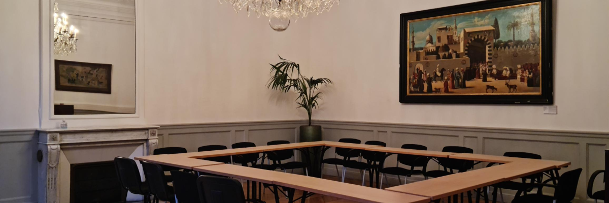Salle avec table, chaises, lustre, peinture, miroir, radiateur et plante. Parquet au sol.
