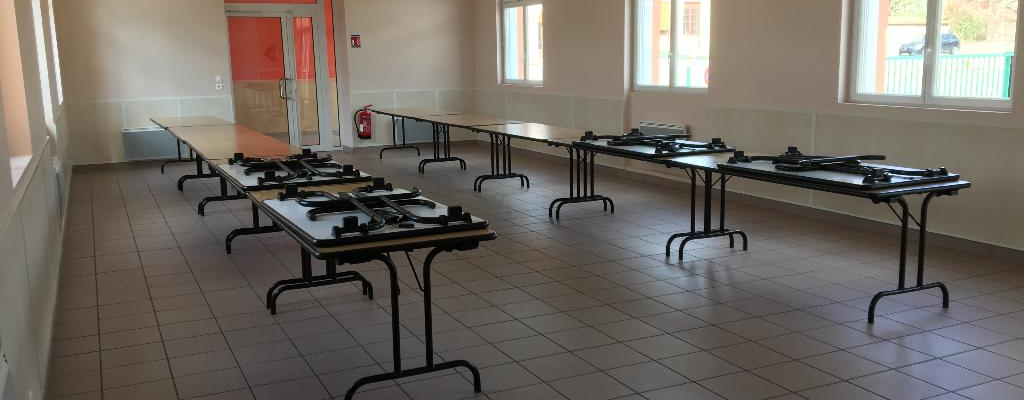 Salle avec tables, chaises, extincteur, porte rouge et fenêtres.