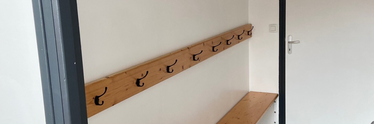 "Vestiaire avec banc, patères et porte dans un couloir."
