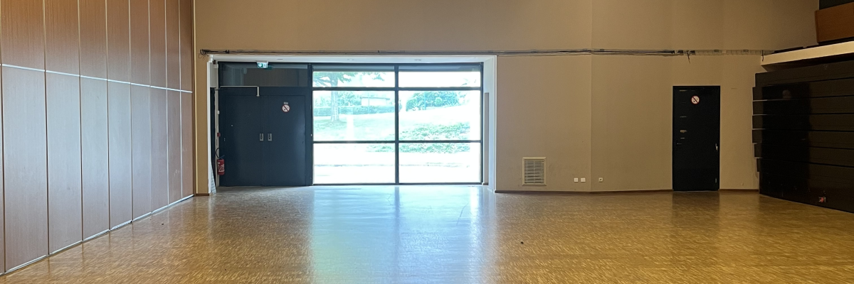 Grande salle avec parquet, lumières au plafond, portes vitrées et murs beiges.