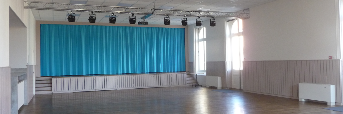 Salle avec parquet, rideau bleu, projecteurs suspendus et murs blancs.