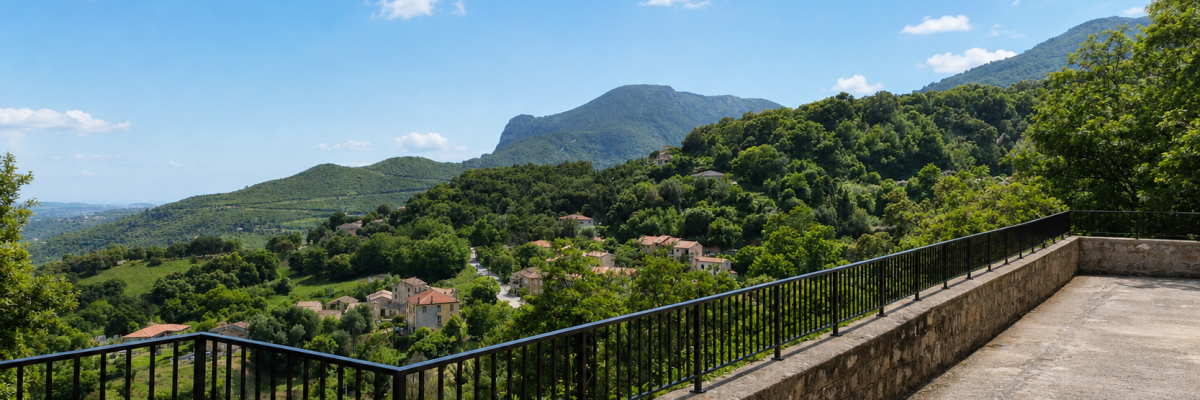 Chemin de pierre avec garde-corps métallique, vue sur village et montagnes.