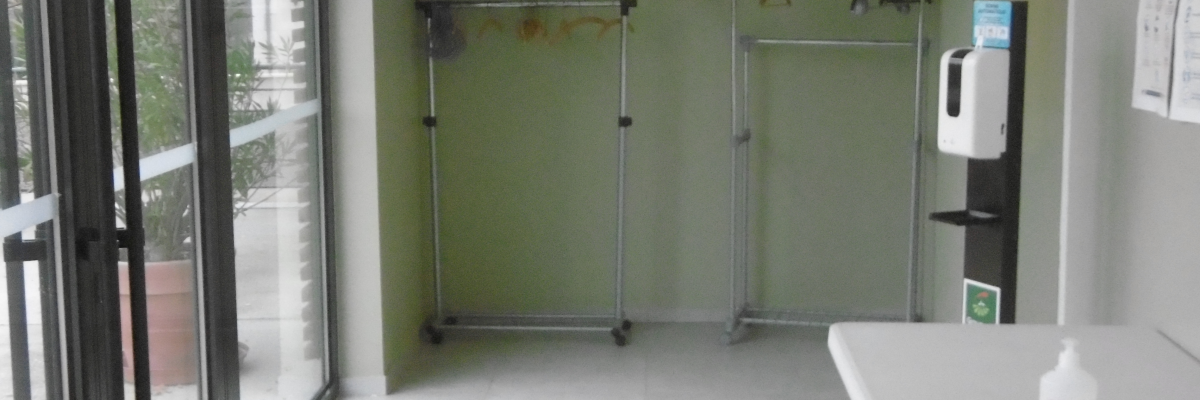 "Salle avec porte vitrée, rack à vêtements, distributeur de gel, table et bouteille de gel."
