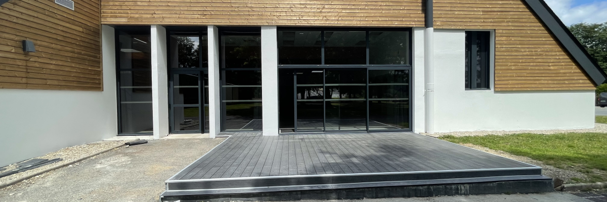 Bâtiment moderne avec façade en bois et verre, terrasse en bois.