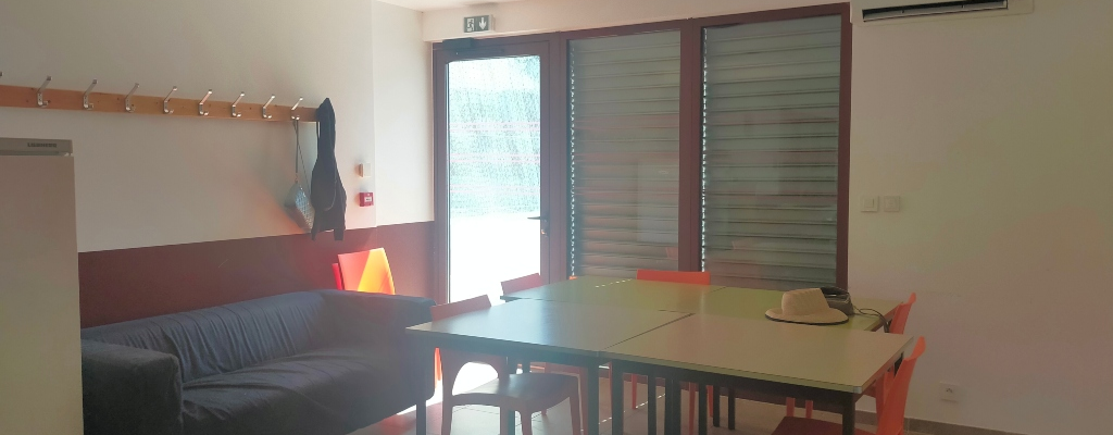 Pièce avec canapé, table, chaises, porte-manteau, climatiseur et porte vitrée.