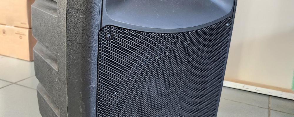 Haut-parleur noir avec roues sur sol carrelé.