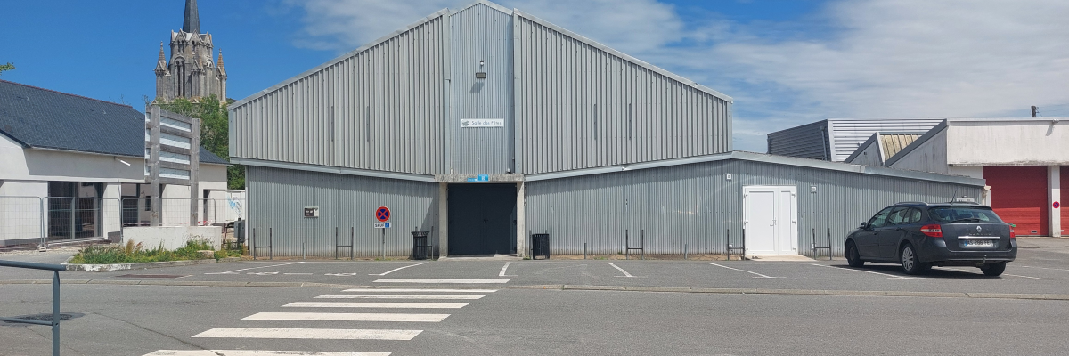 Bâtiment industriel avec voiture, église en arrière-plan, parking et passage piéton.