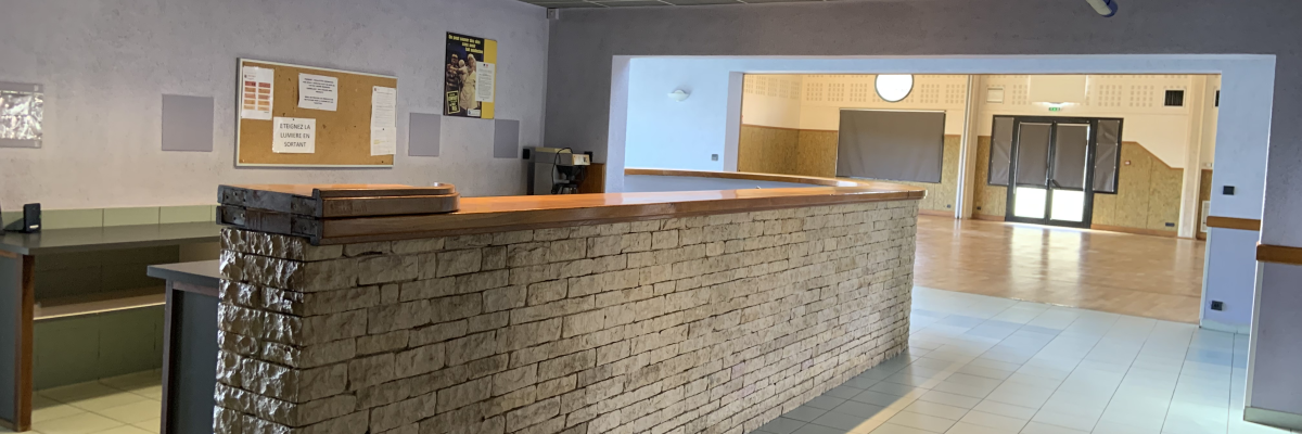 Réception avec comptoir, tableau d'affichage, banc et porte vitrée.