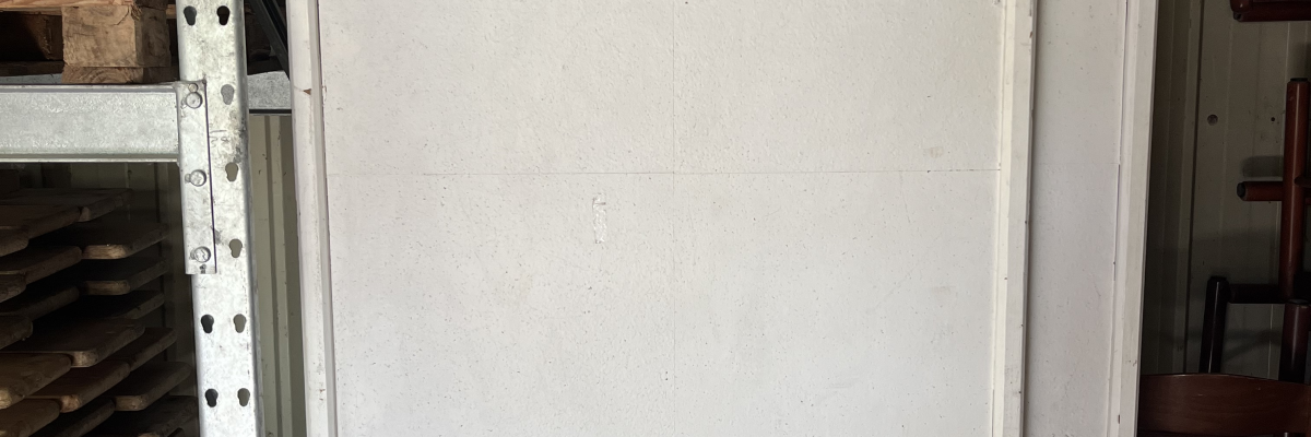 Table pliante blanche avec pieds en métal, rangée contre un rack de stockage.