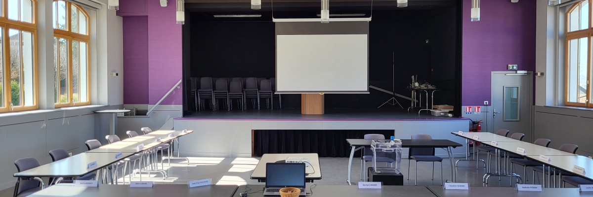 Salle de classe avec tables, chaises, tableau blanc, ordinateur portable, projecteur et écran.