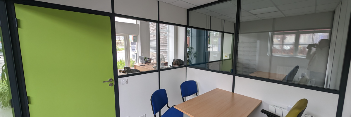 Bureau avec table, quatre chaises, mur vert, cloison vitrée, vue sur open-space.