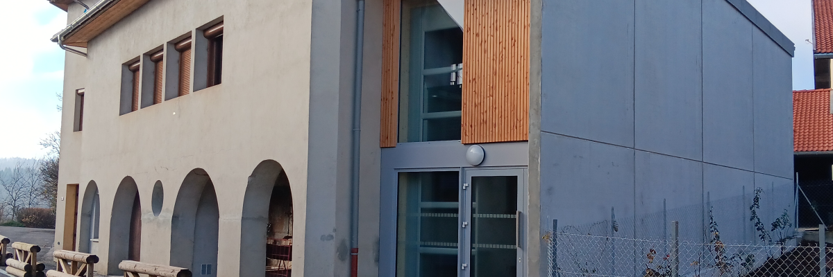 Bâtiment avec façade mixte, arches, grandes fenêtres et porte vitrée.