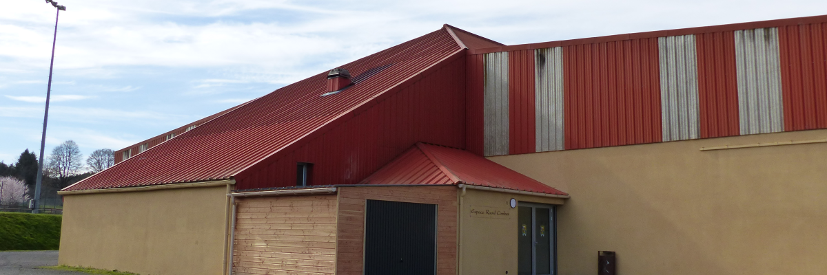 Bâtiment industriel avec toit rouge, murs beiges et bruns, porte de garage et entrée principale.