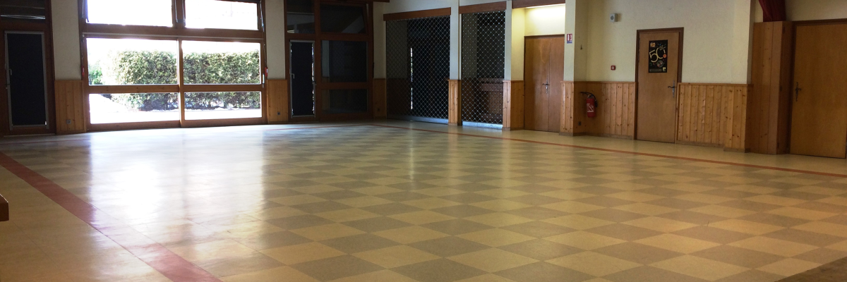 Salle vide avec carrelage en damier, portes et grande fenêtre.