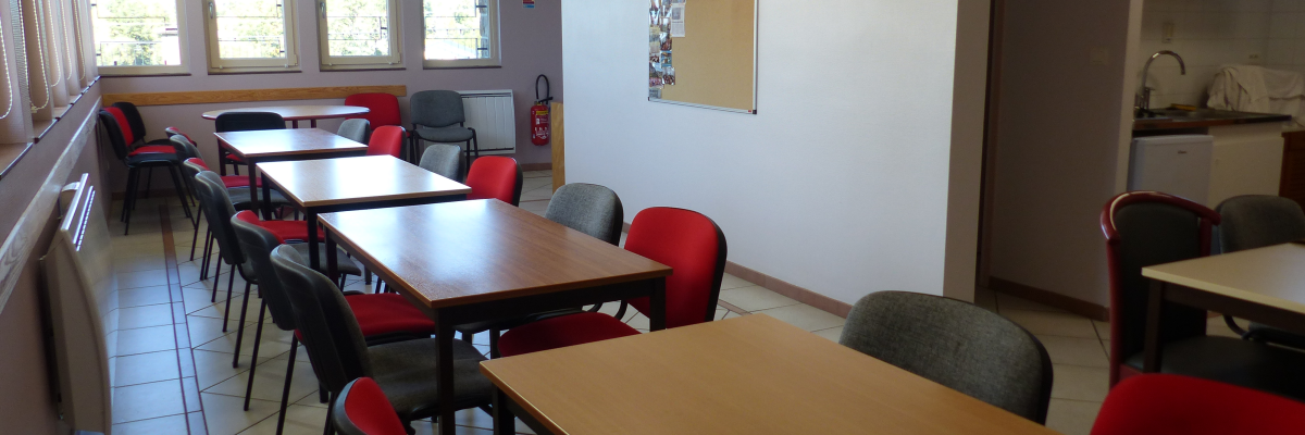 Salle avec tables, chaises, tableau d'affichage, évier et armoire.