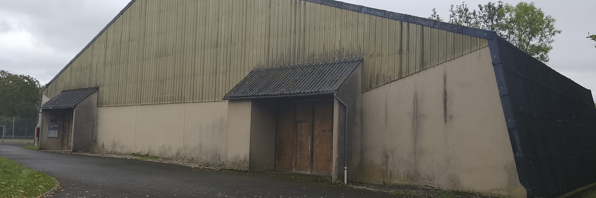 Bâtiment industriel avec murs en béton et tôle, toiture en pente, deux portes de garage et une petite entrée.